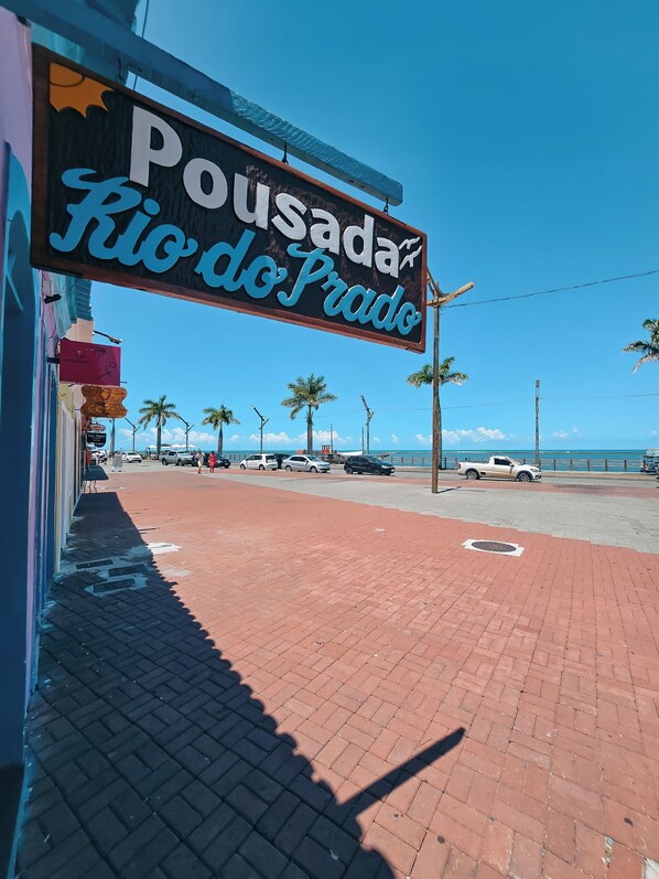 Letrero de 'Pousada Rio do Prado' con una vista despejada de la playa y palmeras al fondo.
