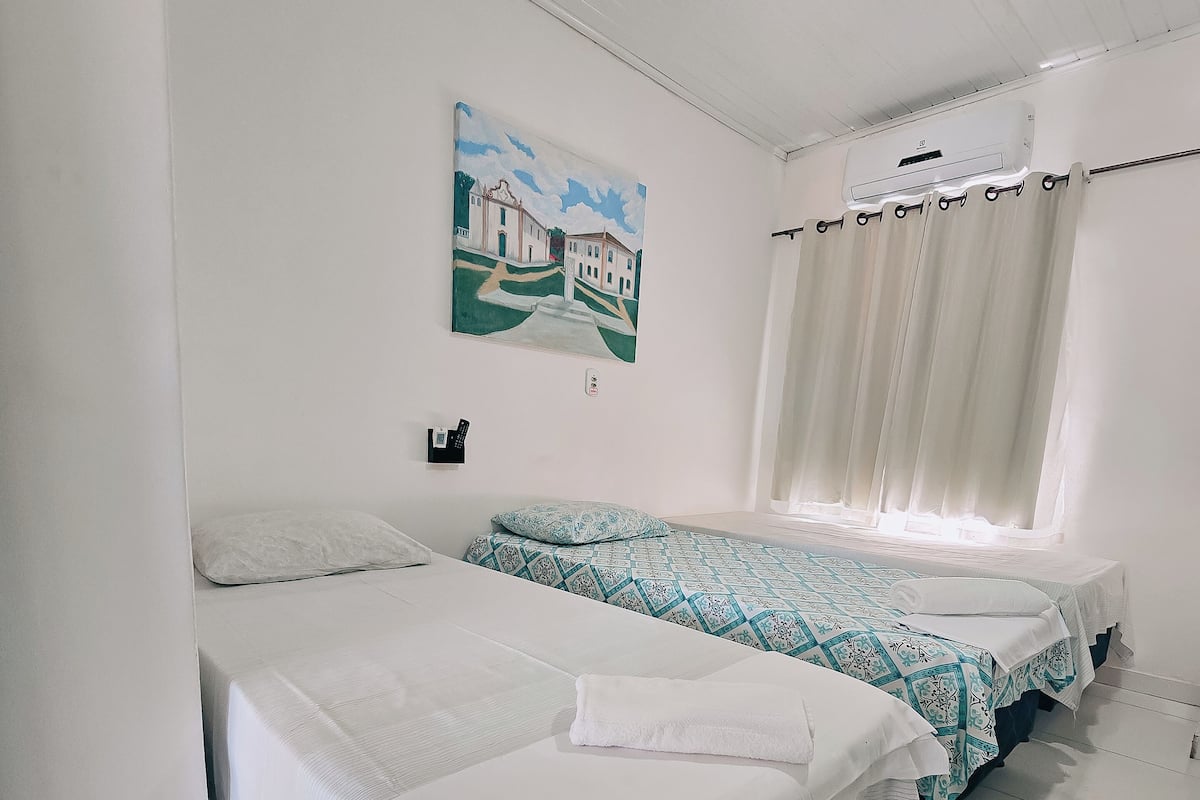 A hotel room with two beds, a painting on the wall, and a ceiling fan.