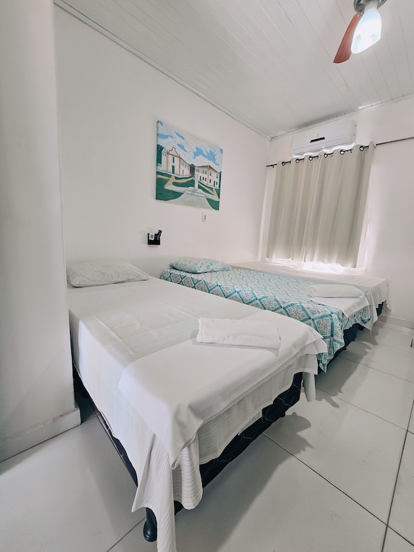 A hotel room with two beds, a painting on the wall, and a ceiling fan.