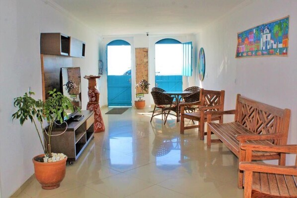 A spacious living area with a TV, wooden furniture, and potted plants.