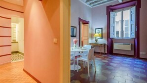 A room with a tiled floor, a dining table with chairs, a small table with a lamp, and a window with shutters. - CAMPO DE' FIORI PINKY HOUSE (Rome)
