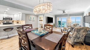 A modern kitchen with a central island, a dining area with a chandelier, and a view of the ocean through large windows. - 723- Beautiful, TOP FLOOR UNIT w/ Stunning Views! Free Beach Service (Destin)