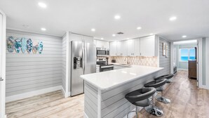 A modern kitchen with a central island, bar stools, and a view to the outside. - 723- Beautiful, TOP FLOOR UNIT w/ Stunning Views! Free Beach Service (Destin)