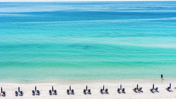 A beach with rows of sun loungers and a person walking along the shore. - 723- Beautiful, TOP FLOOR UNIT w/ Stunning Views! Free Beach Service (Destin)
