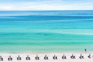 A beach with rows of sun loungers and a person walking along the shore. - 723- Beautiful, TOP FLOOR UNIT w/ Stunning Views! Free Beach Service (Destin)