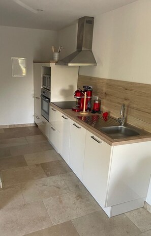 Una cocina moderna con armarios blancos, un lavamanos de acero inoxidable y una campana extractora.