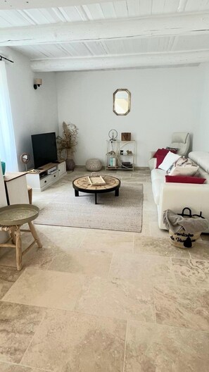 Una sala de estar con una mesa redonda, un sofá, un televisor y un suelo de baldosas de piedra.
