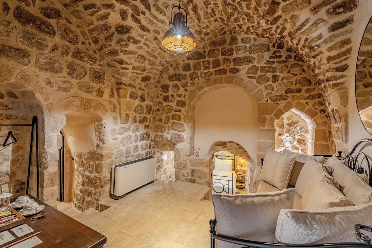 A stone-walled room with a fireplace, a sofa, and a table with writing materials.