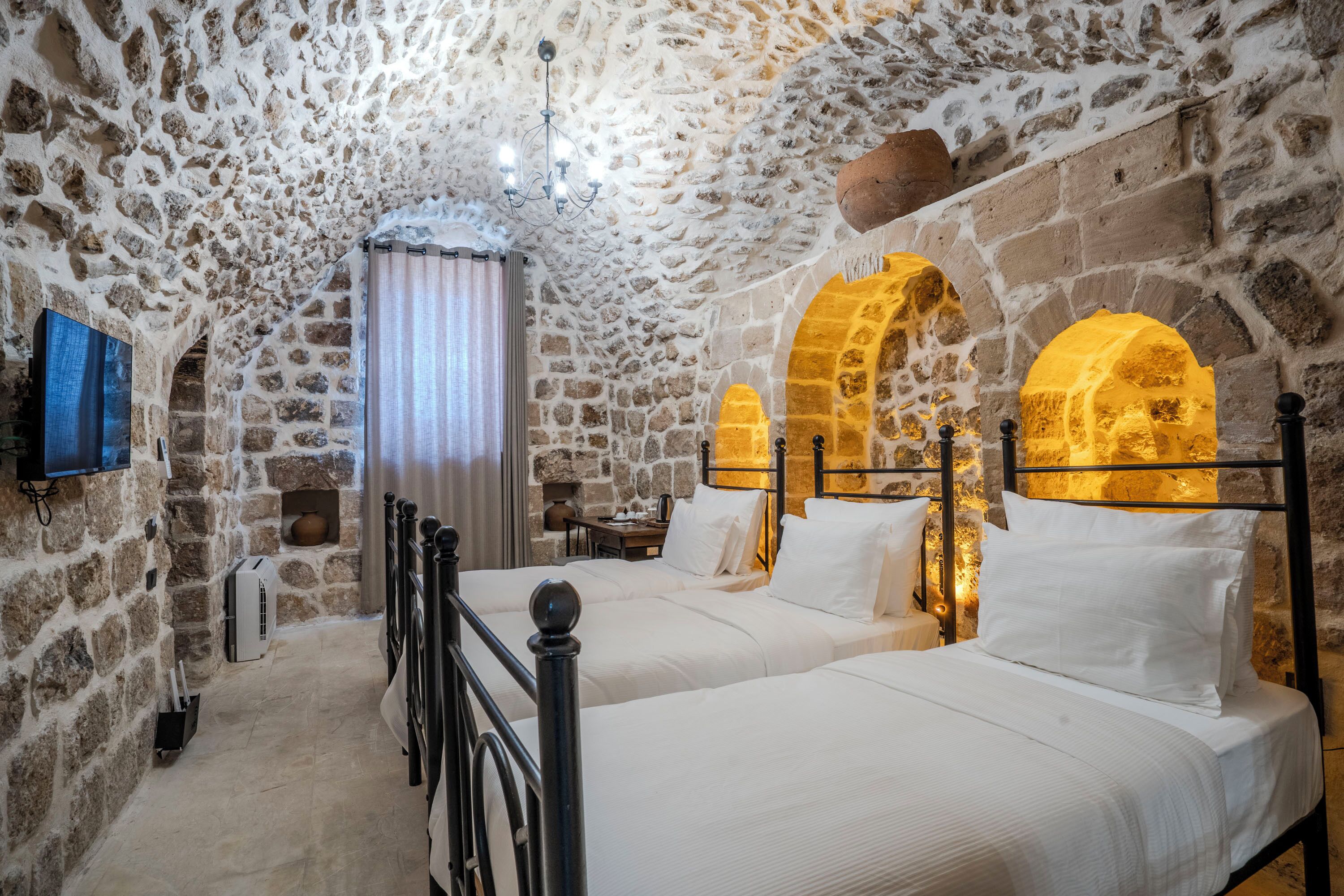 A stone-walled bedroom with two beds, a television, and a window with curtains.