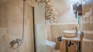 A bathroom with a stone wall, a white toilet, a sink with a round basin, and a shower with a handheld showerhead.