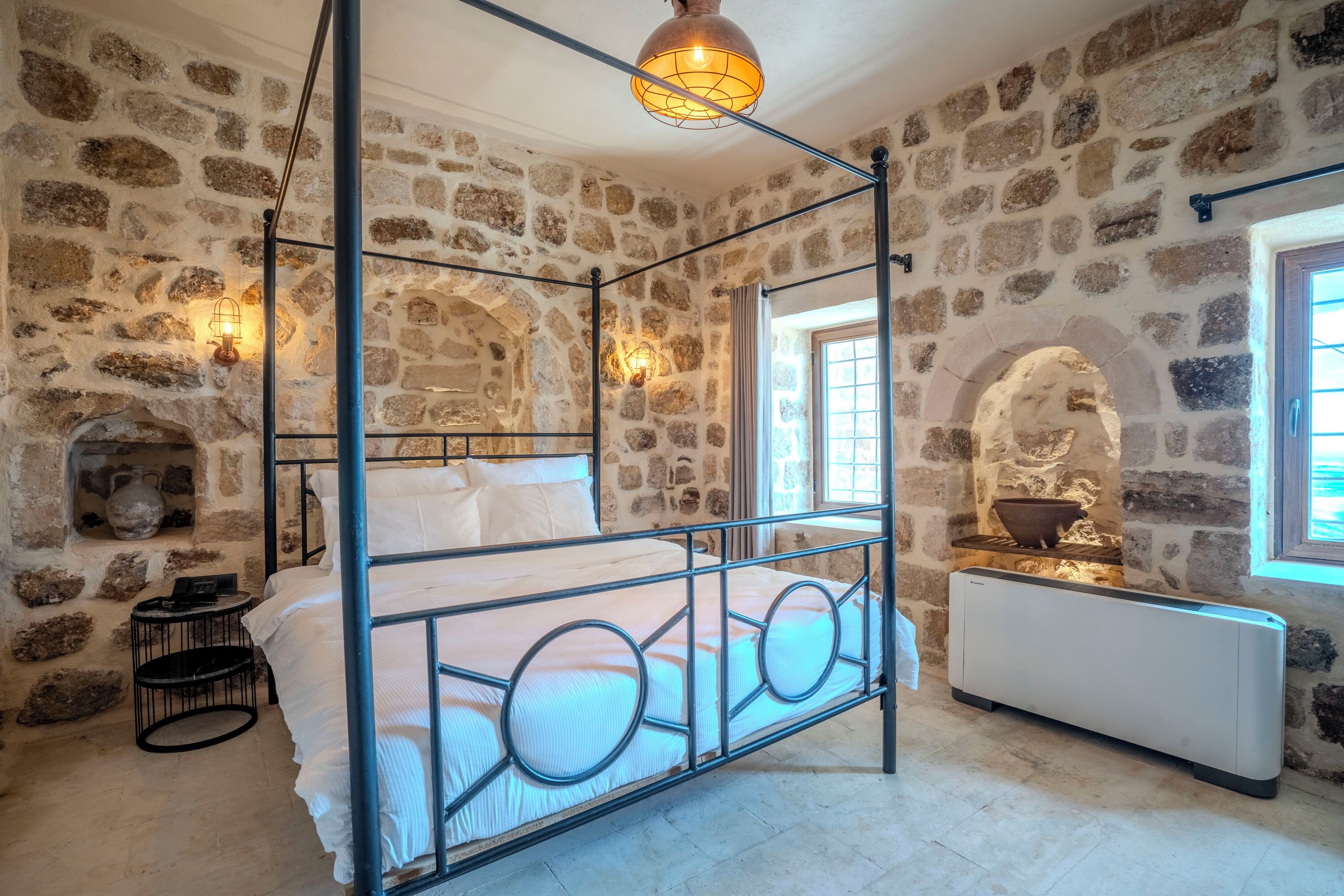 Un lit à baldaquin avec un mur en pierre en arrière-plan, une cheminée en pierre et un radiateur.
