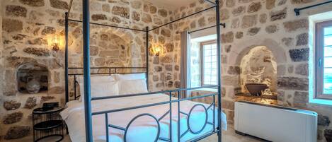 Un lit à baldaquin avec un mur en pierre en arrière-plan, une cheminée en pierre et un radiateur.