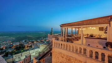 Une terrasse sur le toit offrant une vue sur la ville en contrebas, un espace repas avec des tables et des chaises, et un escalier menant à la terrasse.