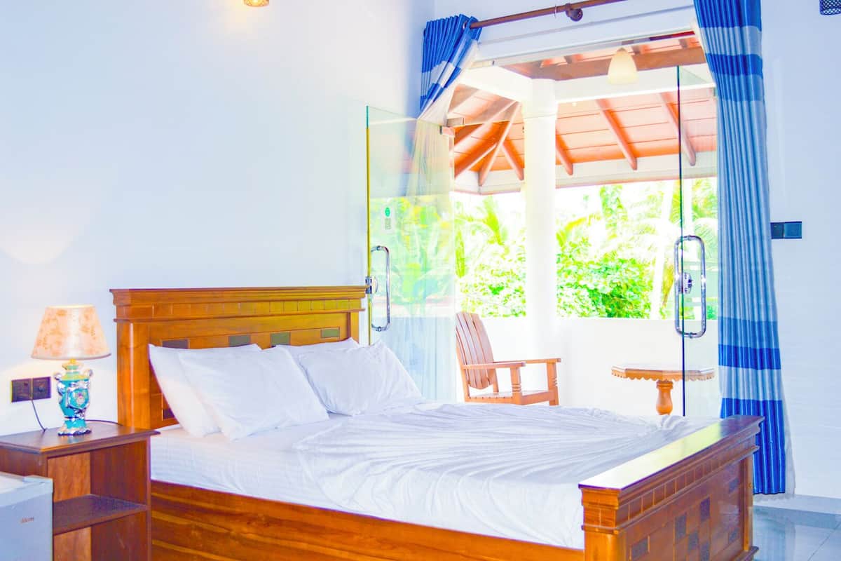 Un lit avec une tête de lit en bois, une table de chevet avec une lampe et une chaise près d’une fenêtre avec des rideaux.