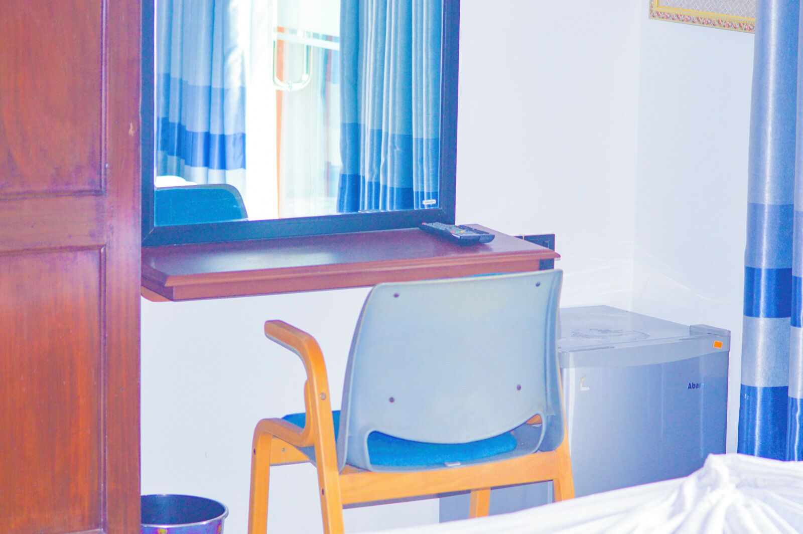 A room with a bed, a desk with a computer, a chair, and a trash bin.