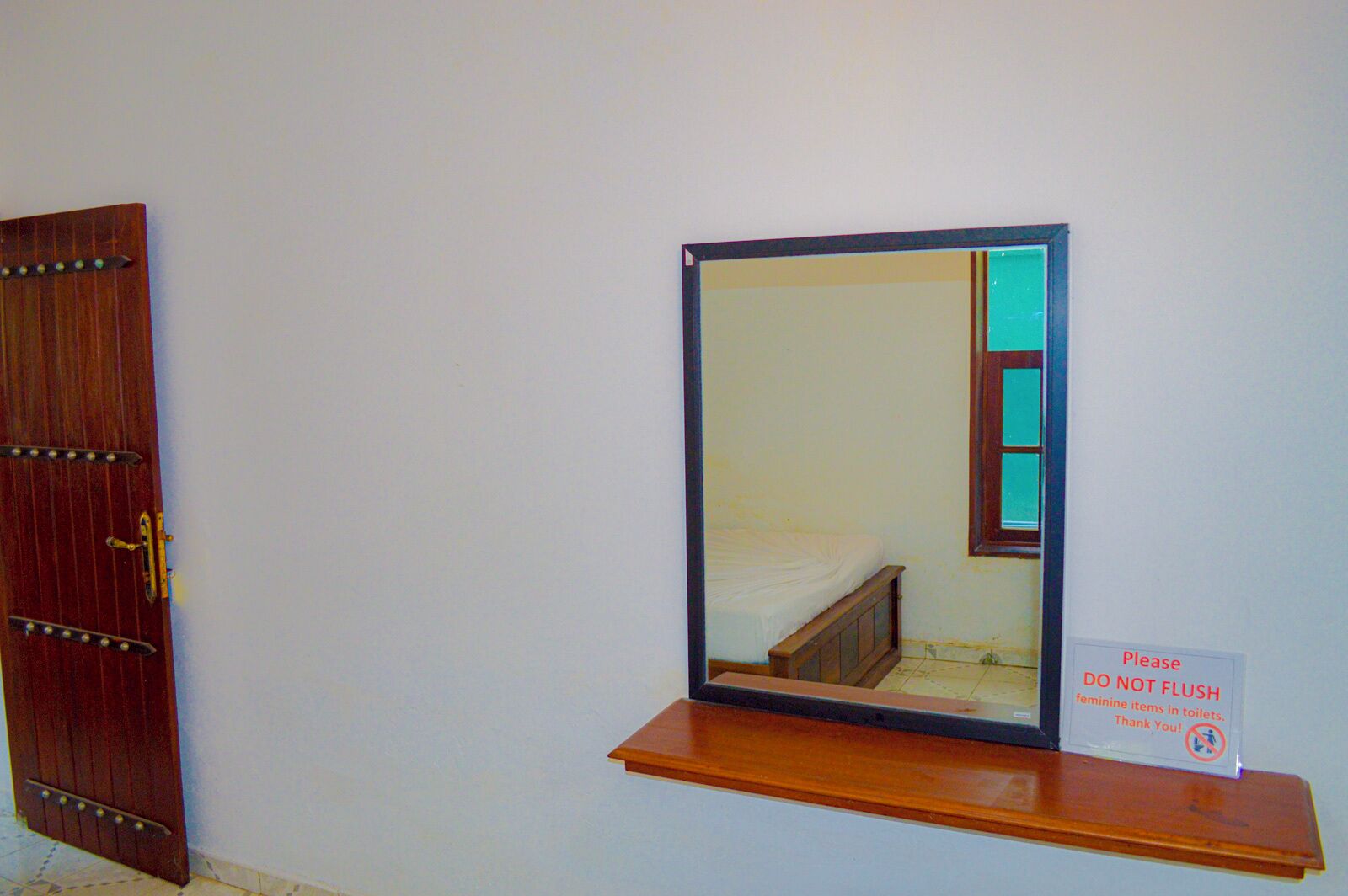 A mirror on a wooden shelf with a sign below it.