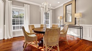 Une salle à manger avec une table ronde, des chaises en osier, un lustre et un grand miroir.