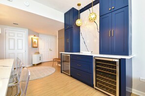 A modern kitchen with dark blue cabinets, a wine cooler, and a dining area with a round rug and clear chairs.