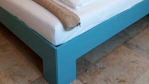 A neatly made bed with white linens and a beige throw blanket, a teal accent wall, and a painting of a coastal scene. - Your bed by the sea (Koksijde)