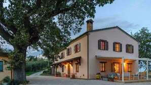 A two-story house with a covered porch and outdoor seating area. - Casale Partemio 8 Marche Holiday Villas (Cartoceto)