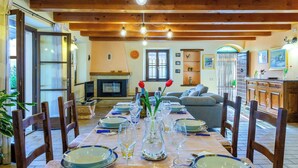 A dining area with a long table set for a meal, wooden chairs, a fireplace, and a cozy living room in the background. - Casale Partemio 8 Marche Holiday Villas (Cartoceto)