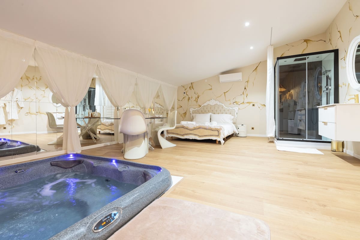 A modern bedroom with a large bed, a glass shower enclosure, and a hot tub.