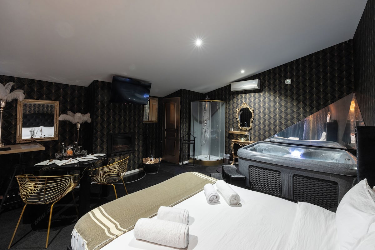 A hotel room with a bed, a desk with a chair, a shower area, and a jacuzzi.