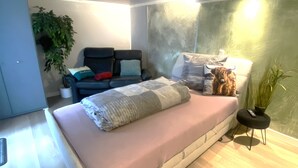 Ein modernes Schlafzimmer mit einem Bett, einer Couch, einem kleinen Tisch und einer Topfpflanze.