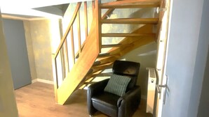 Ein Zimmer mit einer Holztreppe, die zu einer oberen Ebene führt, einem schwarzen Ledersessel mit Kissen und einer weißen Tür.