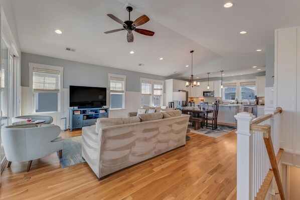 A spacious living room with a large sofa, a television, and a ceiling fan. - 5 Star Kure | Ocean View Retreat w/ Community Pool & Private Beach Access! (Kure Beach)
