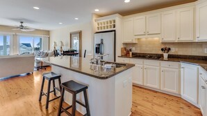 Una cocina moderna con gabinetes blancos, encimera de granito y una isla central con taburetes.
