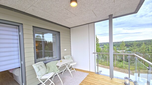 A balcony with a table and chairs, a view of the landscape, and a large window.