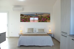 A bedroom with a bed, bedside tables, a wardrobe, and a wall-mounted air conditioner. - Residence in Pozzo San Nicola  (Stintino)