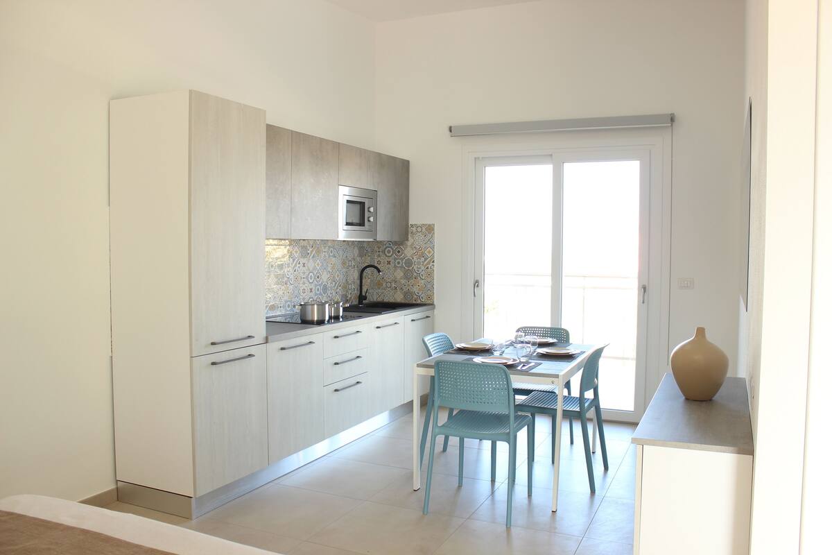 A modern kitchen with white cabinets, a microwave, and a dining area with blue chairs.