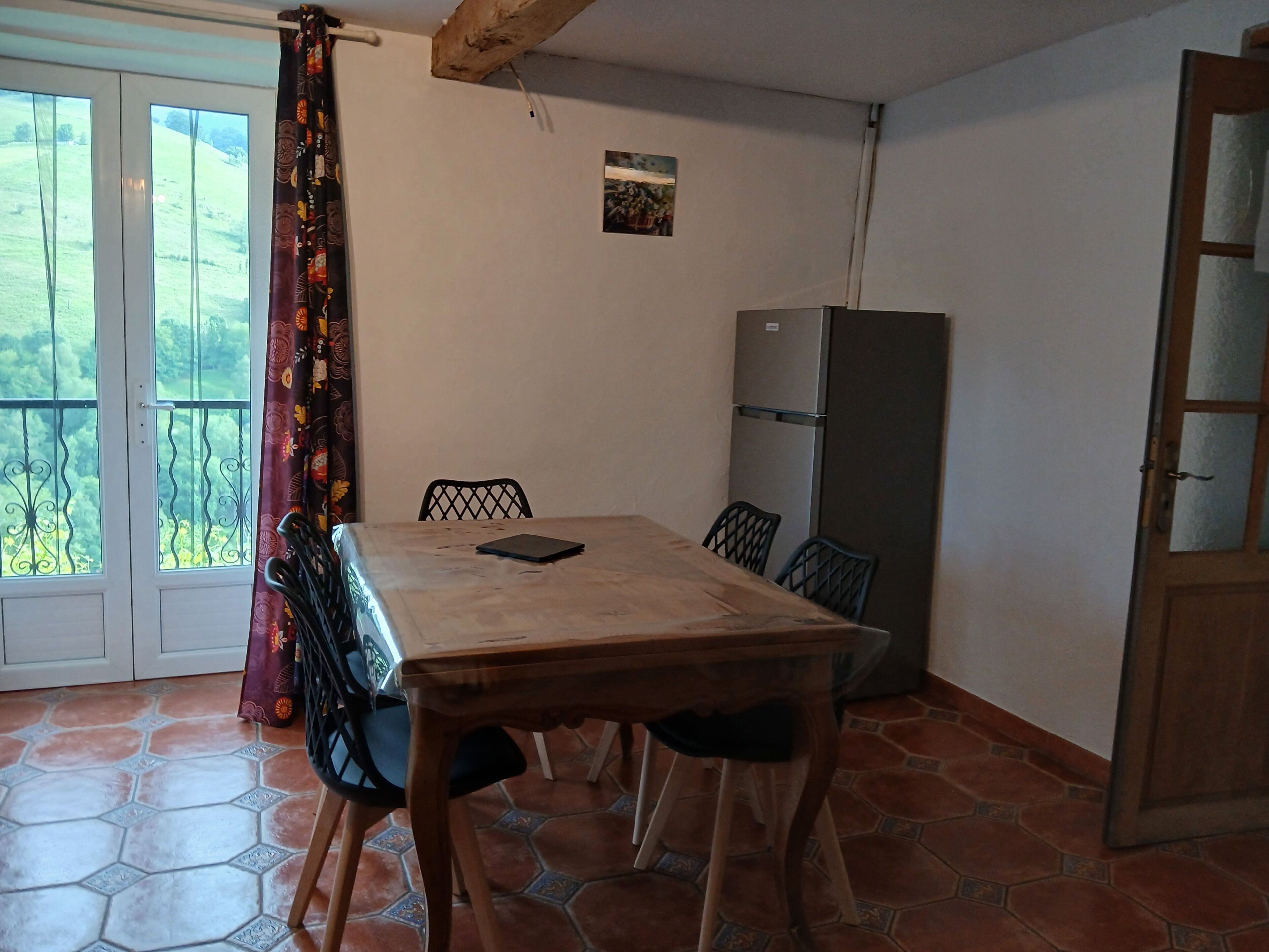 Een eetgedeelte met een tafel, stoelen, een koelkast en uitzicht door een deur.
