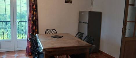 Een eetgedeelte met een tafel, stoelen, een koelkast en uitzicht door een deur.