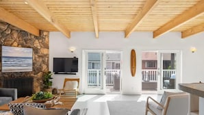 Un salon spacieux avec un mur en pierre, un téléviseur à écran plat et un plafond en bois.