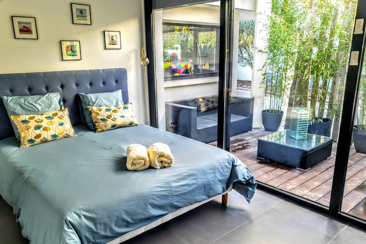 A bedroom with a bed, pillows, and a view of an outdoor balcony with potted plants.