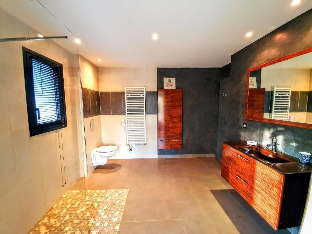 A modern bathroom with a large mirror, wooden vanity, and a tiled floor.