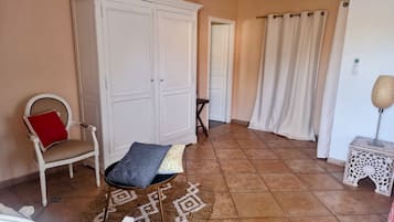 A room with a white wardrobe, a chair with a red cushion, a patterned rug, and a small table with a lamp.