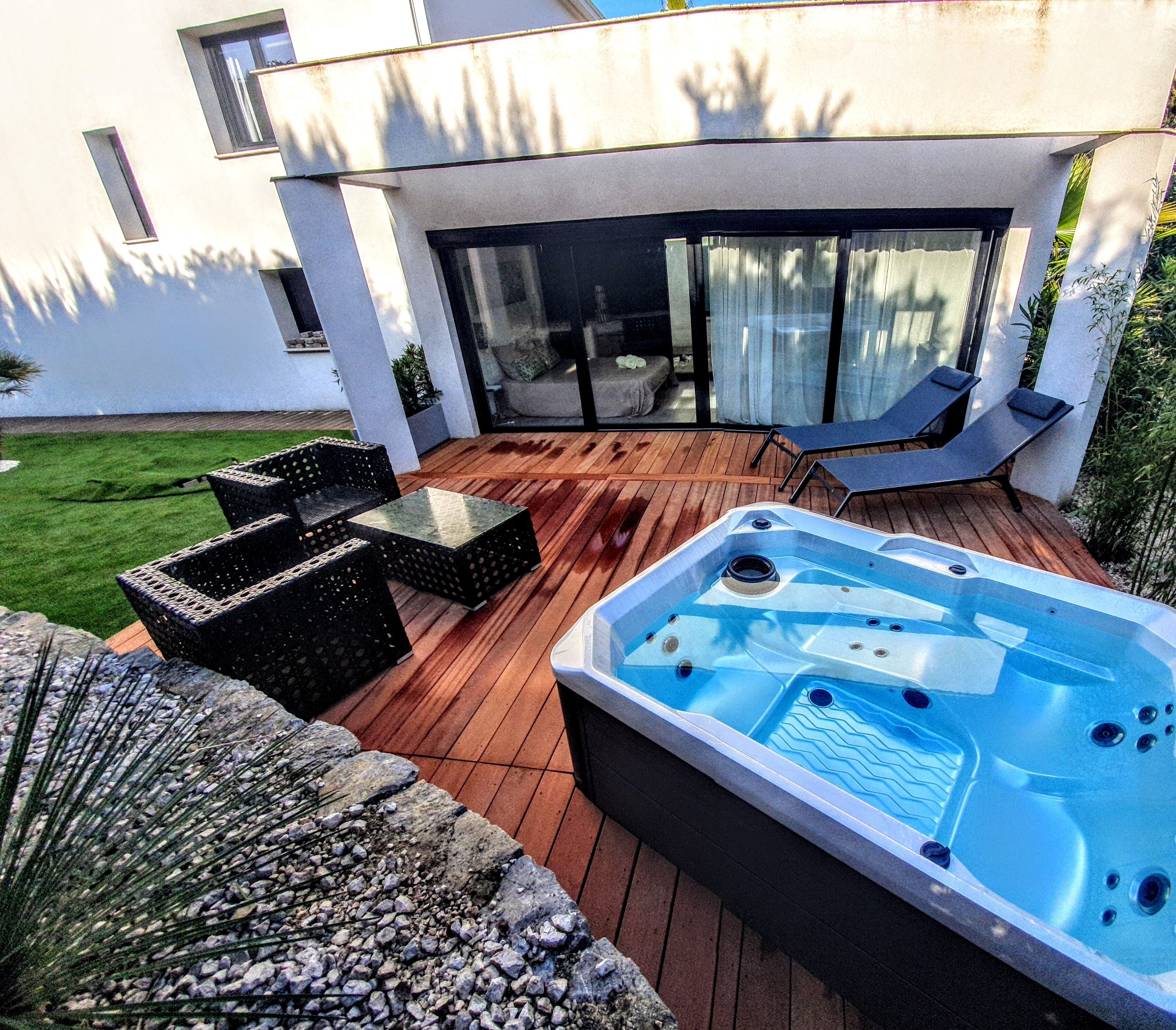 Una terrazza esterna moderna con idromassaggio, poltrone relax e una porta vetrata che dà su un patio.