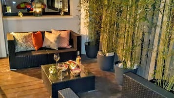 A cozy outdoor seating area with a sofa and a coffee table, surrounded by bamboo plants and potted plants.