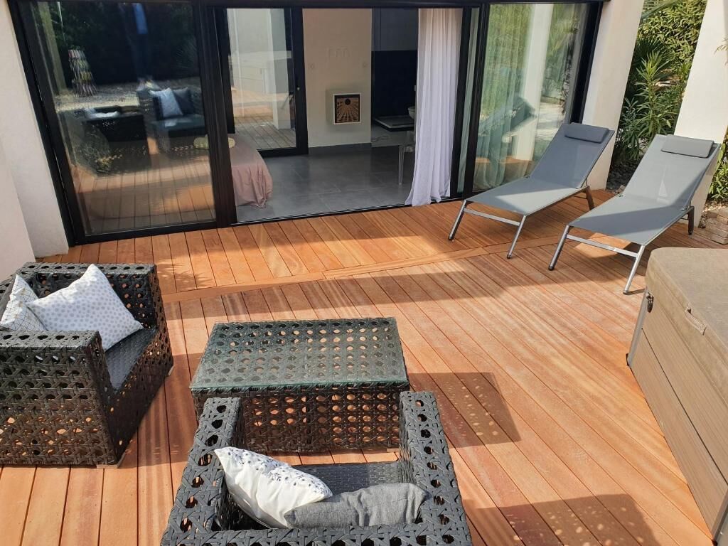 A wooden deck with outdoor furniture, including two wicker sofas and two lounge chairs, and a sliding glass door leading to an interior space.