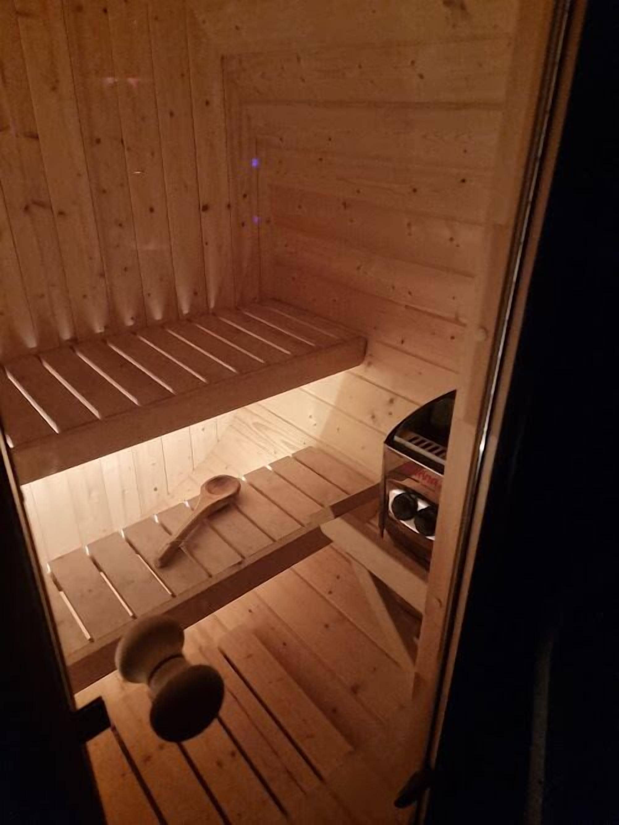 A wooden cabin interior with a bed, a small table, and a shelf with items.