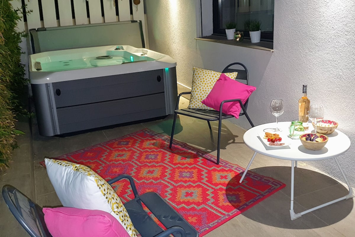 A cozy outdoor seating area with a hot tub, a patterned rug, and a table set with food and drinks.