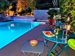 A poolside setting with a table set for dining, a bowl of snacks, and bottles of drinks. - La Villa Blanche (Sanary-sur-Mer)