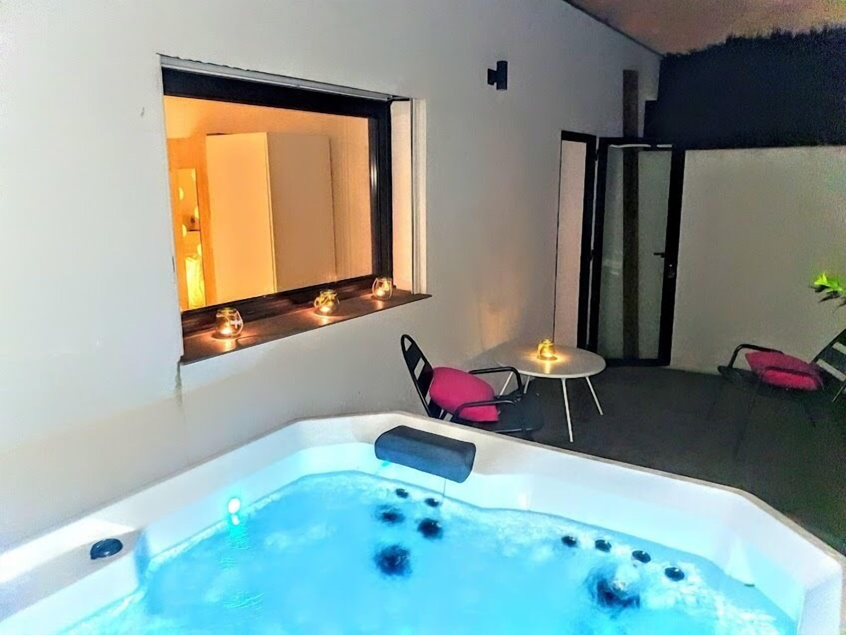 A hot tub with a window above it, a small table with a candle, and a chair.