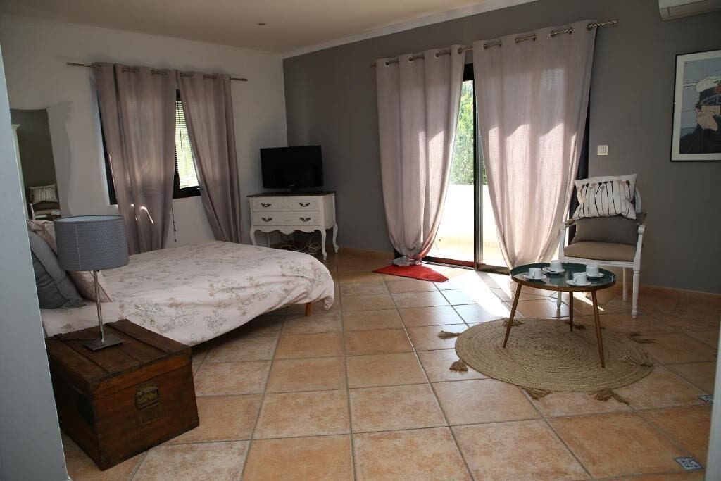 A bedroom with a bed, a TV, a dresser, a chair, and a small table with cups.