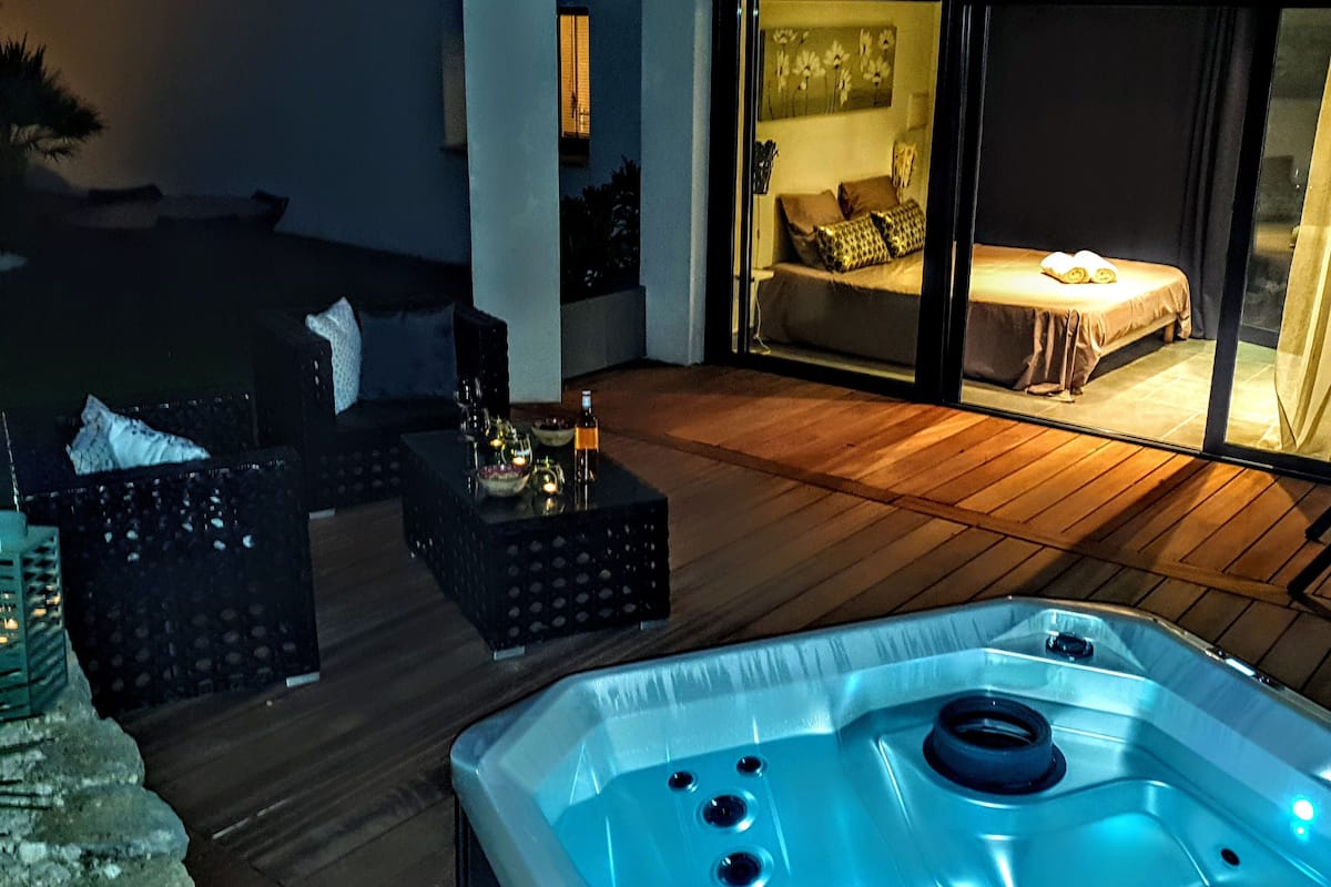 A modern outdoor living area with a hot tub, wooden flooring, and a cozy seating arrangement.