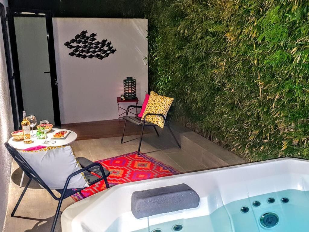 A hot tub area with a table and chairs, a decorative wall, and a small table with drinks.